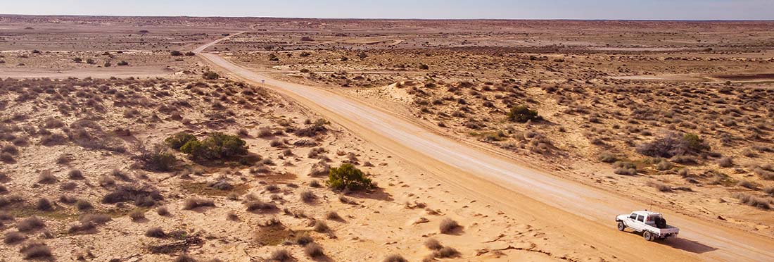 A long dirt road in the outback with a white ute traveling along it
