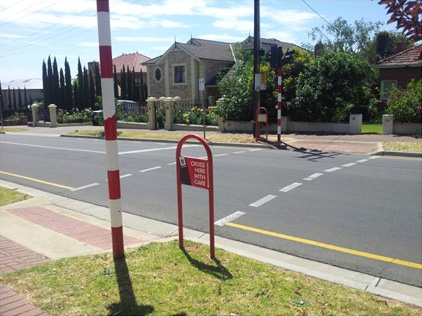 A Koala crossing at the side of a road is seen. The lights are not flashing.