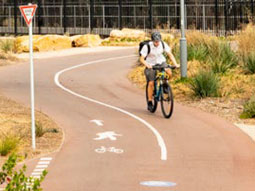 A cyclist in a white shirt bikes down a shared path.